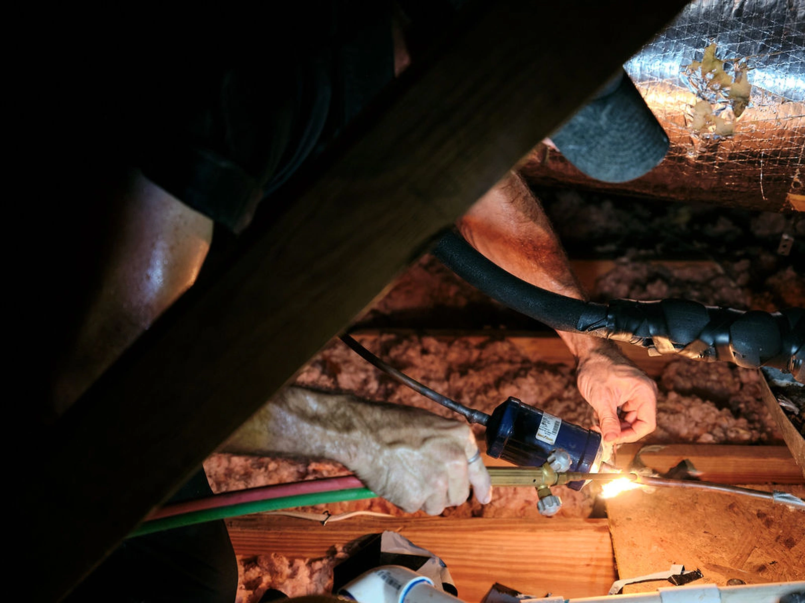 Rooted Heating & Air worker repairing HVAC wiring in an attic