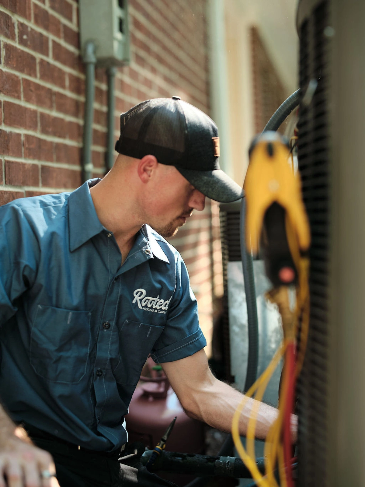 Rooted Heating & Air technician working on a heating system by a brick wall