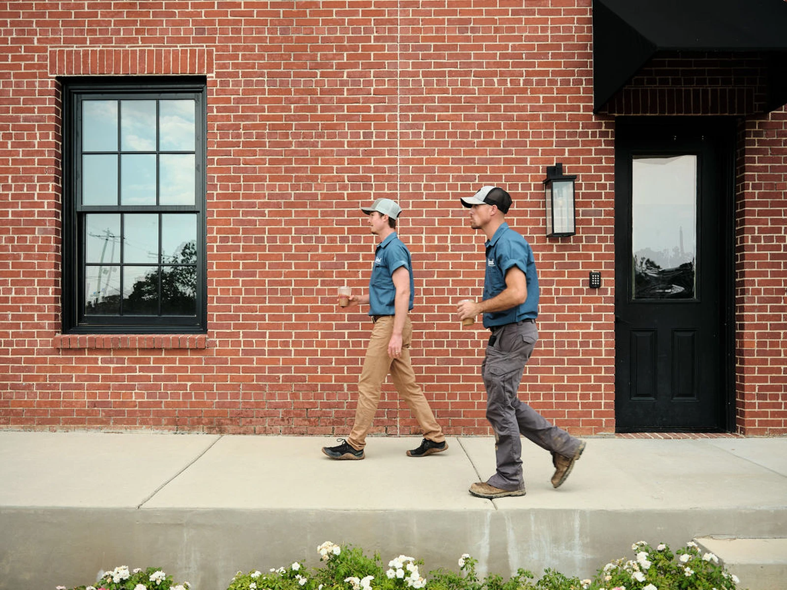 Rooted Heating & Air repair technicians walking past a brick building